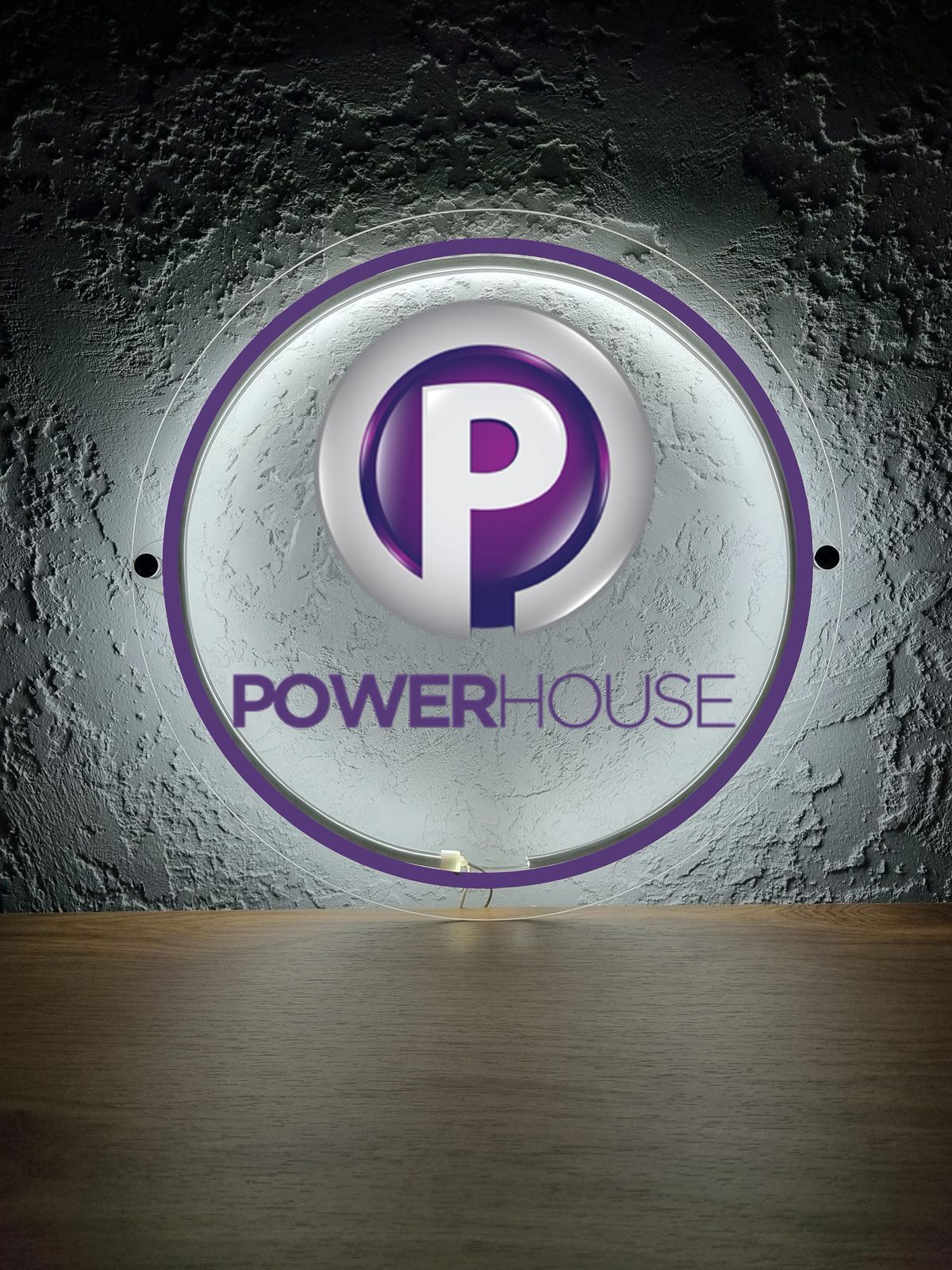 Illuminated round purple and white 'P' logo sign reading POWERHOUSE mounted on textured gray wall above wood table.
