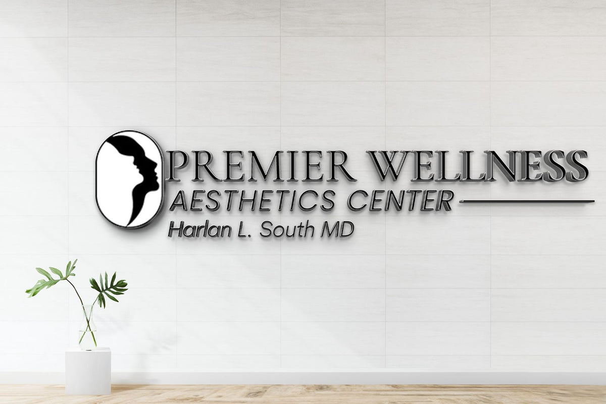 Metallic wall sign PREMIER WELLNESS AESTHETICS CENTER Harlan L. South MD with black oval profile logo on white tile.