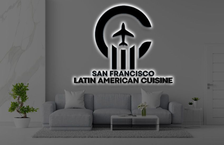 Backlit black logo with airplane in crescent and text SAN FRANCISCO LATIN AMERICAN CUISINE over gray sofa in modern.