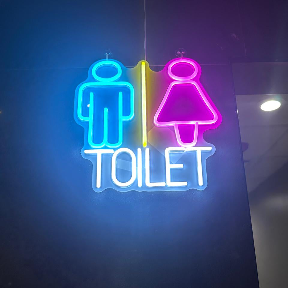 A Volt Signs neon custom sign displays blue male and pink female icons with a yellow divider and TOILET signage