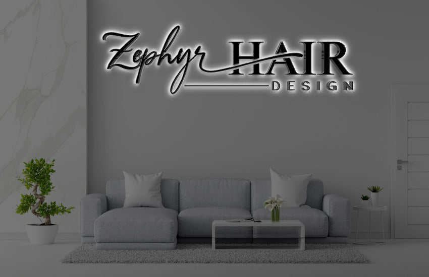 Illuminated 'Zephyr HAIR DESIGN' logo sign on gray wall above modern gray sofa, glass coffee table, potted plants.
