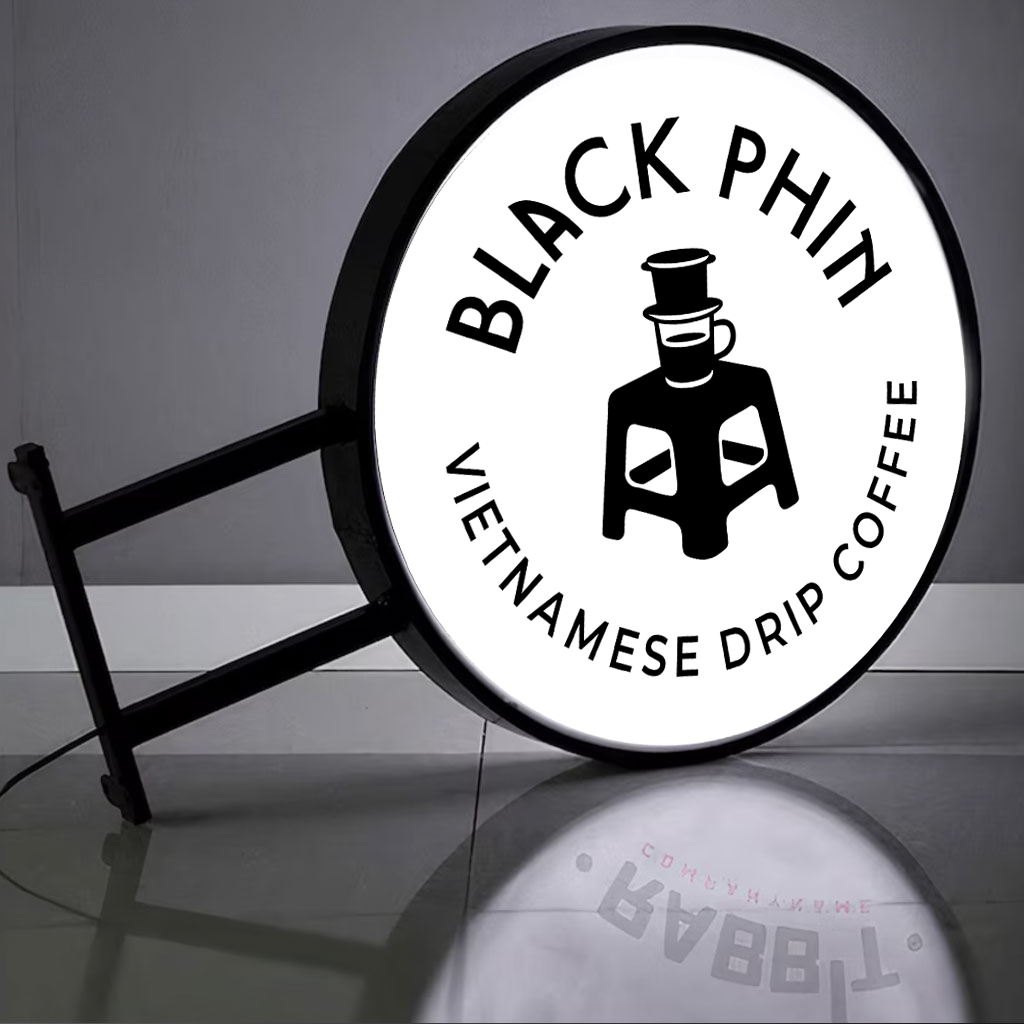 Illuminated round sign 'BLACK PHIN' 'VIETNAMESE DRIP COFFEE' with phin-and-stool logo reflected on glossy tile floor.