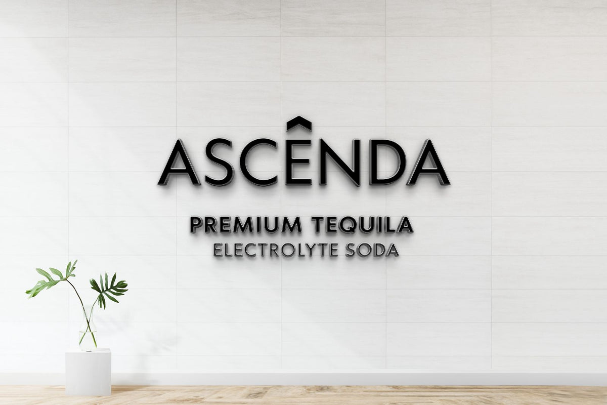 Black 3D sign "ASCÊNDA" with "PREMIUM TEQUILA" and "ELECTROLYTE SODA" on white tiled wall, glass vase with green leaves.