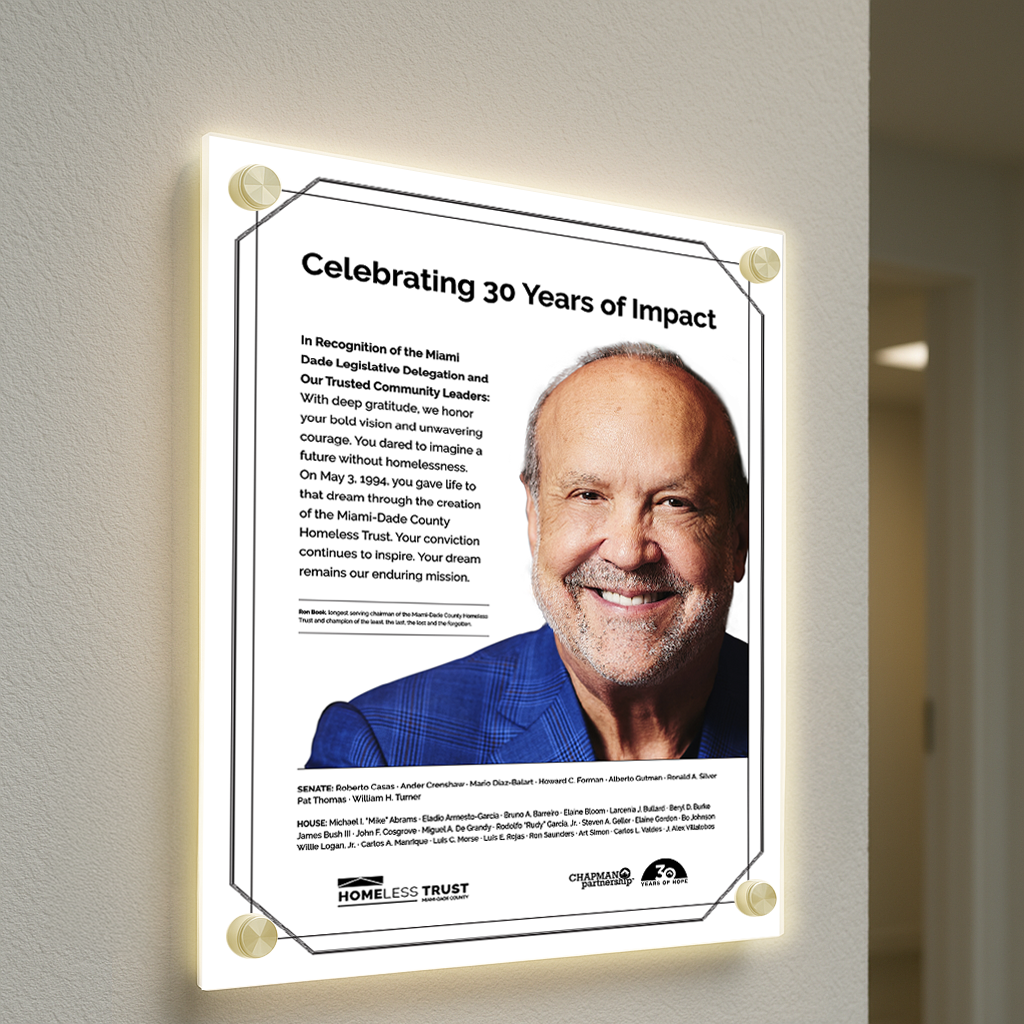 A backlit plaque reading 'Celebrating 30 Years of Impact' shows a smiling man in a blue blazer and Homeless Trust logo.