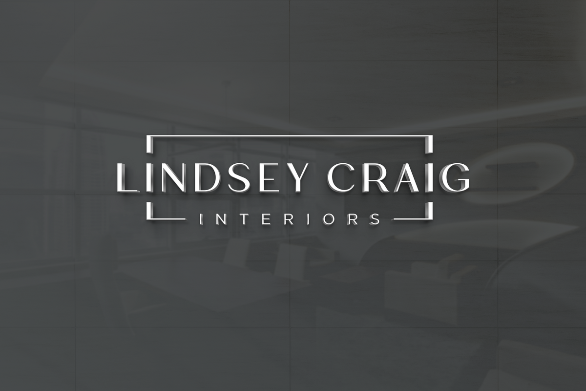 White 3D lettering 'LINDSEY CRAIG' framed by white corner brackets with 'INTERIORS' below on dark gray reflective wall.