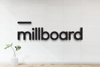 Black 3D letters spelling 'millboard' mounted on white tiled wall with black rectangular accent and glass vase.