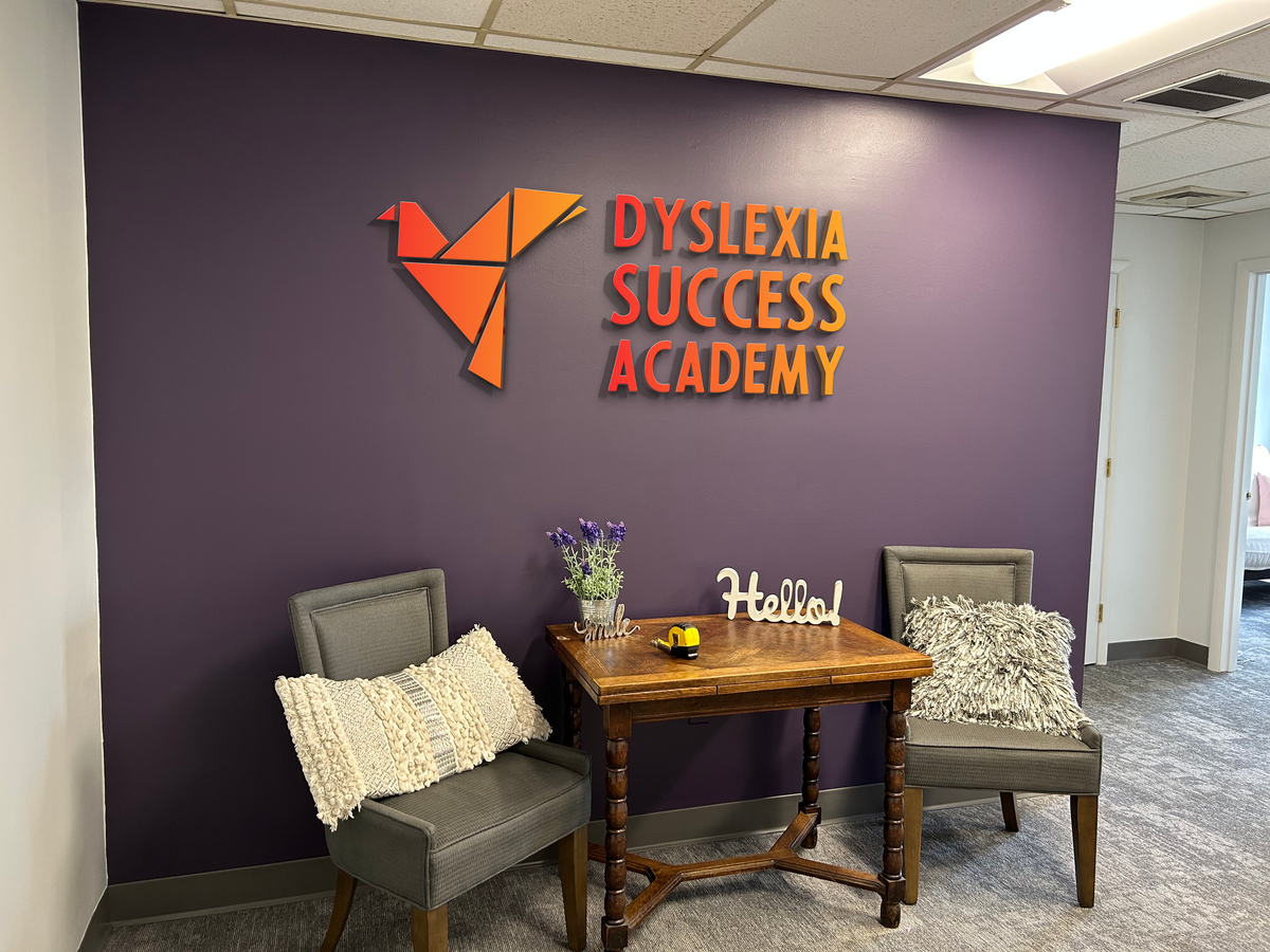 A purple lobby wall features an orange Volt Signs custom sign reading Dyslexia Success Academy with seating