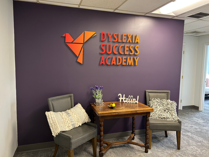 A purple lobby wall features an orange Volt Signs custom sign reading Dyslexia Success Academy with seating