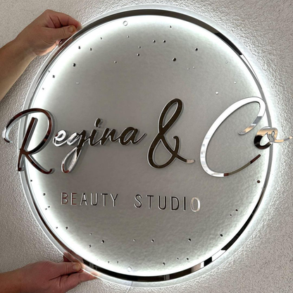 Illuminated round mirror-acrylic beauty studio sign: 'Regina & Co' script with 'BEAUTY STUDIO', hands.